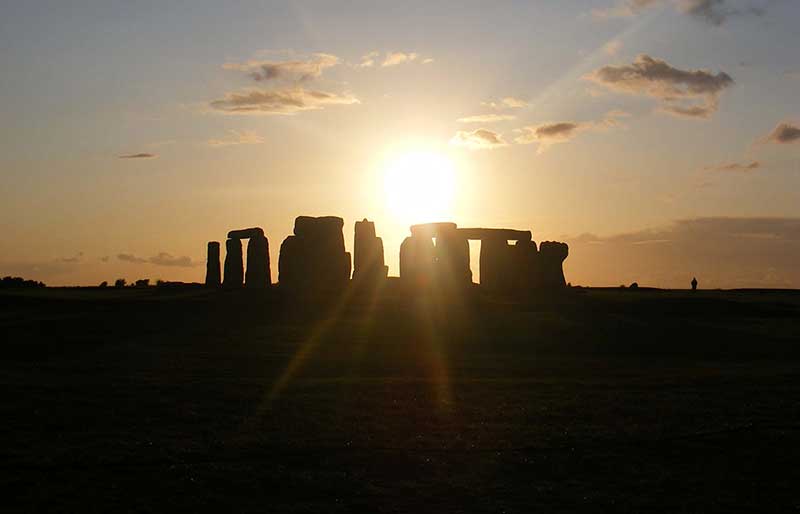 In silhouette with sun rising over the stones.
