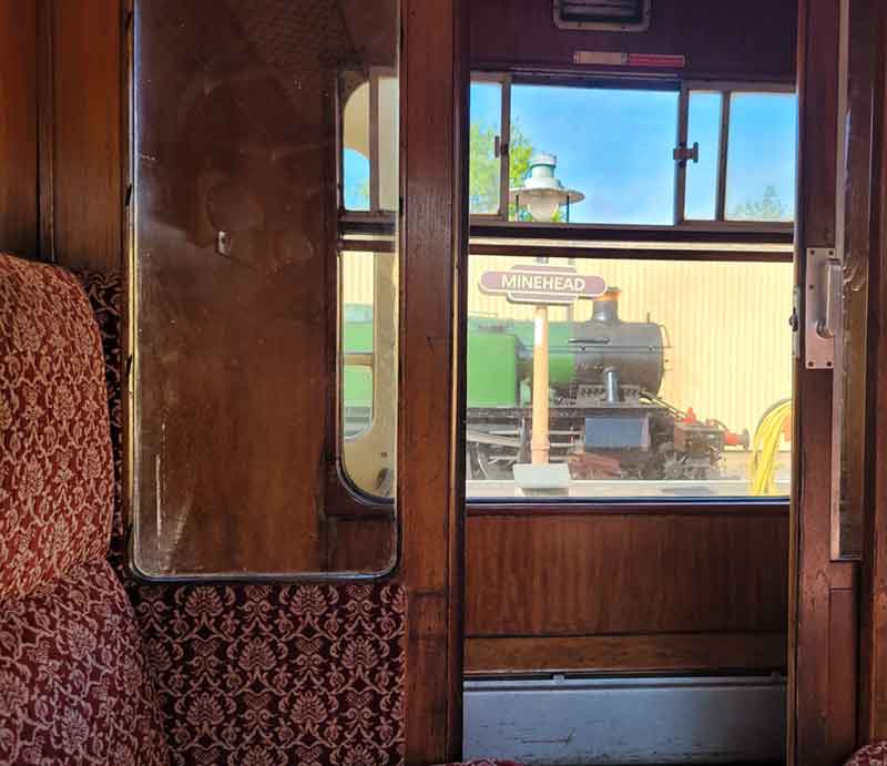Looking through carriage window to opposite platform with steam locomotive.